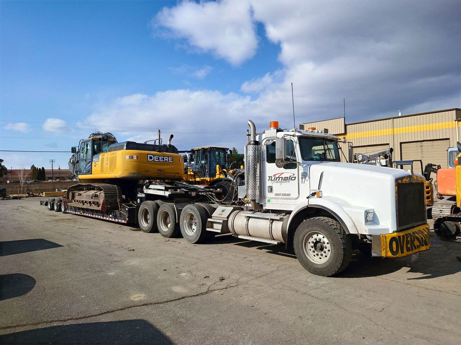Kenworth tractor with an oversize banner hauling a John Deere 350G excavator on a lowboy