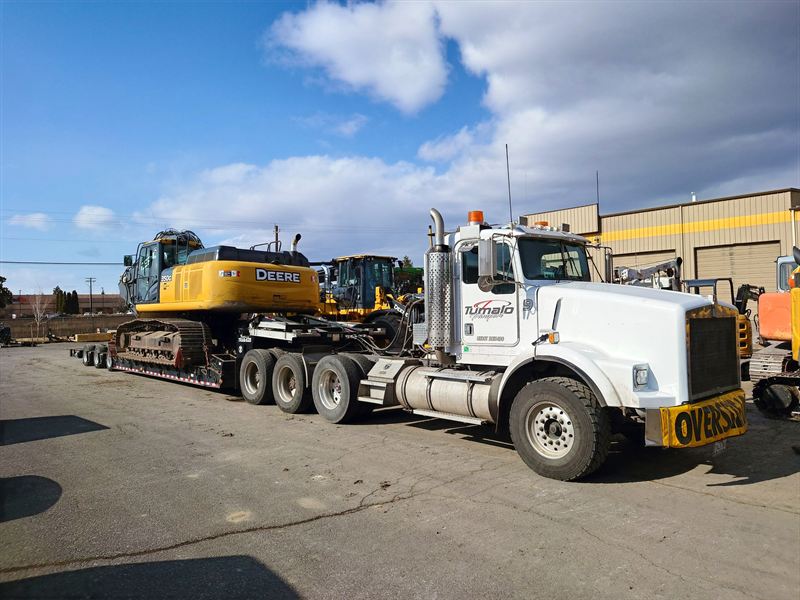 Kenworth tractor with an oversize banner hauling a John Deere 350G excavator on a lowboy trailer